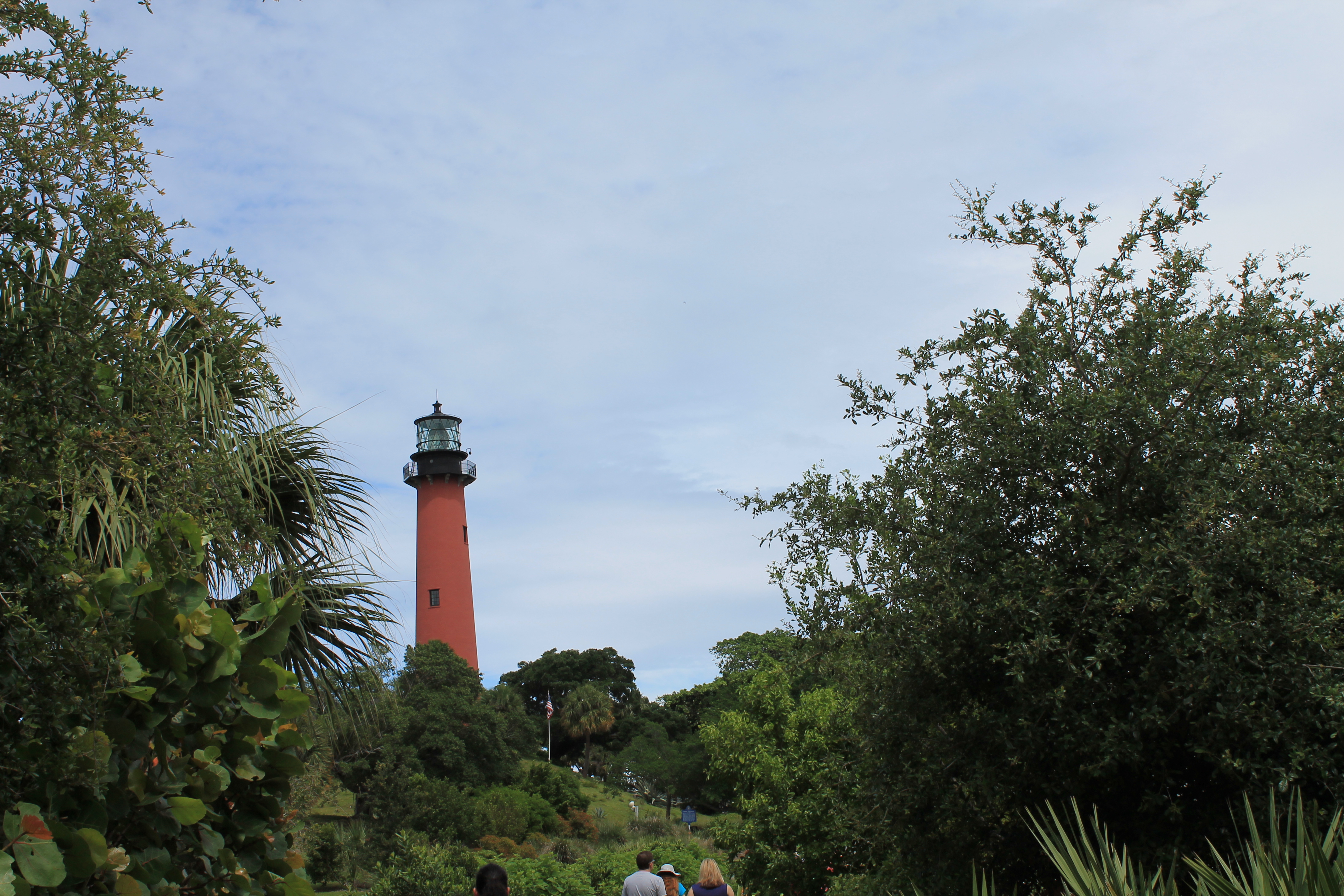 This lighthouse photo is beautiful… It's a bright red lighthouse set against a brilliant blue sky surrounding by green nature.